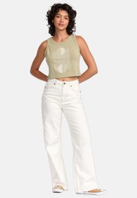 Afgeknot olijfgroen tanktop met een wit abstract patroon, gecombineerd met hoge witte flare jeans en canvas sneakers.