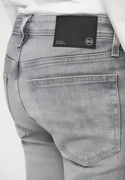 Graue Denim-Jeans mit einem nachhaltigen schwarzen Zellulose-Patch, Gesässtaschen und dezenten Nähdetails. Strukturierter Stoff mit einem abgetragenen Finish.