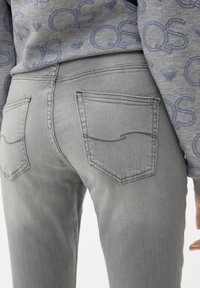 Jeans de mezclilla gris con un diseño ajustado, que cuentan con dos bolsillos traseros y sutiles acentos de costura. La textura parece suave y ligeramente desgastada.