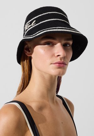 Chapeau bob à rayures noires et blanches en tissu tissé, avec un large bord et des accents brodés. Texture douce, forme ronde.