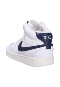 Sneaker bianco in pelle alta con accenti blu navy, punta arrotondata, superficie testurizzata e un logo Nike prominente sul tallone.