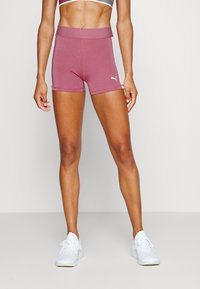 Shorts de sport courts en rose poussiéreux, fabriqués dans un tissu flexible avec une taille haute, arborant un petit logo blanc sur le côté.