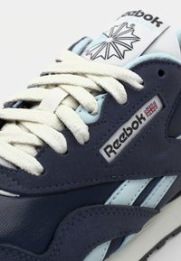Baskets Reebok classique en bleu marine et bleu clair. Présentent un cuir texturé, des rayures contrastantes et des lacets crème. Logo sur le côté.