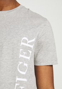 Grå bomulds t-shirt med rund hals og korte ærmer, med hvid tekstgrafik langs venstre side. Blød tekstur, afslappet design.