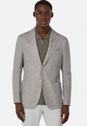Blazer gris claro con dos bolsillos frontales y solapas muesca, llevado sobre un polo verde oscuro. Tejido suave con una textura sutil.