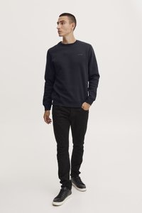 Sudadera azul marino con cuello redondo, puños y dobladillo acanalados, y un pequeño logo de "blend". Combinada con pantalones negros ajustados y zapatillas negras.