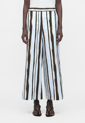 Personne portant un pantalon à jambes larges avec des rayures verticales noires et blanches sur un fond bleu clair, associé à des sandales noires à brides.