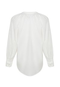 Blouse blanche à manches longues avec encolure et poignets froncés, boutonnée aux poignets, présentée à plat avec le dos vers l'avant.