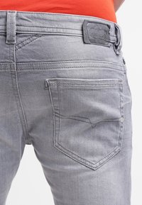 Šedé džíny z denimu s klasickým pěti kapsovém designu, koženým logem na pase a kontrastními švy.