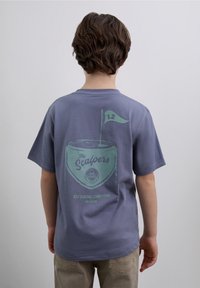 Lila Baumwoll-T-Shirt mit einem Grafikdruck auf der Rückseite, der eine Tasse mit einer Flagge sowie den Text "The Scalers" und "Golf Regional Competition" zeigt.