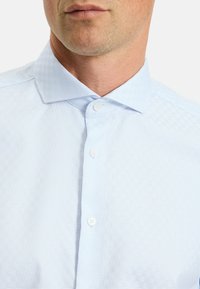 Himmelblaues gemustertes Hemd aus strukturiertem Stoff, mit Button-Down-Kragen und drei weißen Knöpfen an der Vorderseite.