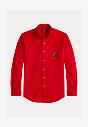 Camisa roja de botones, hecha de algodón, con mangas largas. Cuenta con un bolsillo en el pecho con un diseño de oso bordado. Cuello clásico y botones blancos.