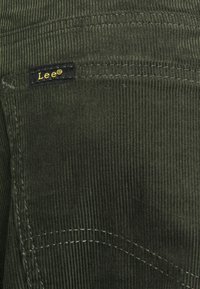 Green corduroy fabric with vertical ridges. Lee® logo tag in black and gold on the side pocket. Features contrasting stitching.