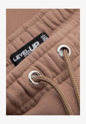 Beżowa tkanina o fakturowanym wykończeniu, z czarną metką oznaczoną "LEVEL UP", srebrnymi oczkami i plecionym sznurkiem.