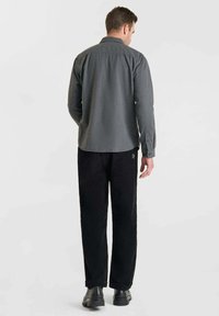 Camisa gris de manga larga con un acabado texturizado, combinada con pantalones de pana negros. Ambas piezas tienen un diseño simple y funcional.