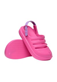Ροζ σανδάλια τύπου slip-on με ανοιχτές σχισμές και ρυθμιζόμενο μωβ λουράκι στο πίσω μέρος, ένα παπούτσι ακουμπά στη υφή της σόλας του.