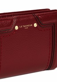 Portafoglio in pelle rossa con superficie testurizzata, dettagli in metallo dorato e cuciture in contrasto. Presenta il logo del marchio impresso sul davanti.