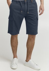 Shorts cargo bleu marine avec une ceinture à cordon de serrage ajustable, poches avant et poches cargo sur les côtés. Tissu en coton avec une finition texturée.