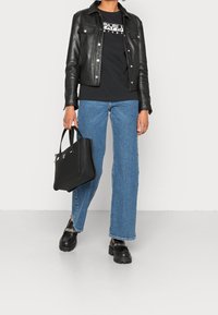 Sort læderjakke over en sort grafisk t-shirt, blå vide bukser, sort håndtaske og kraftige sorte loafers med sølvdetaljer.