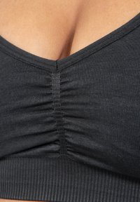 Mustat ribbed bralette, jossa on V-mallinen kaula-aukko, keskellä poimutettu sauma ja sileä pinta. Ei näkyviä koristuksia.