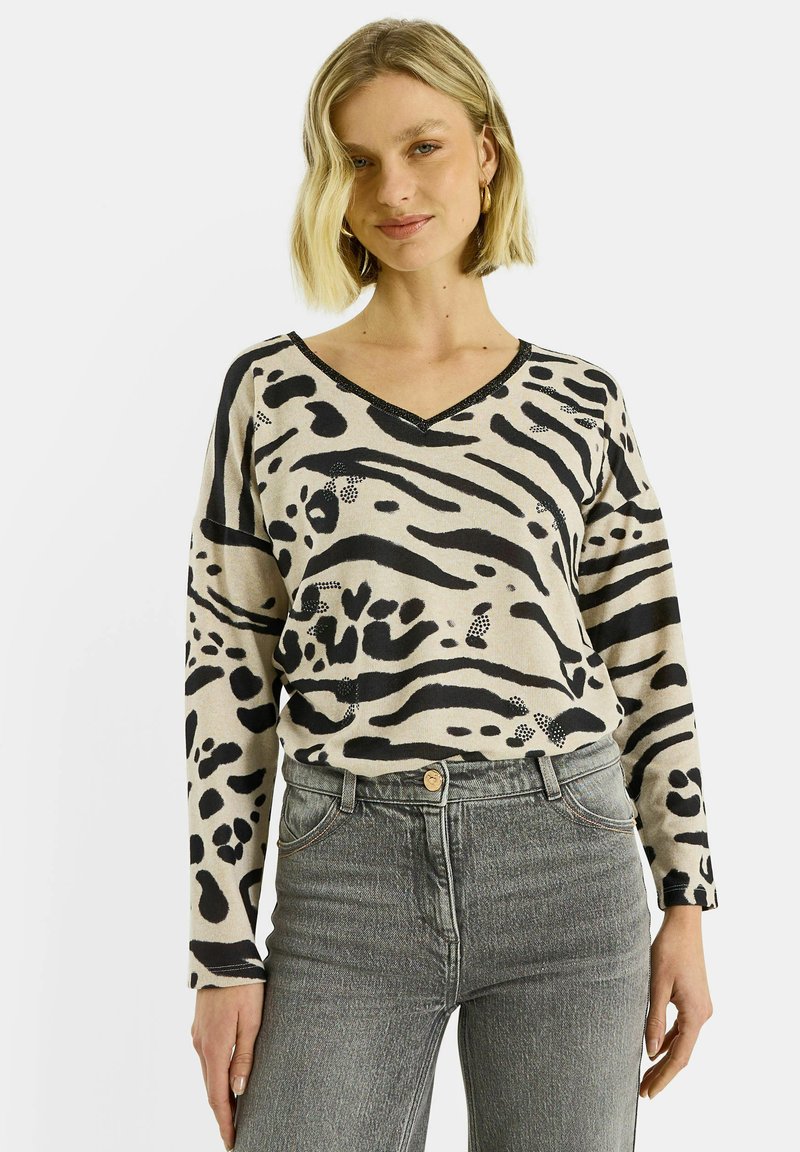 Suéter beige con estampado animal negro, escote en V y mangas largas, combinado con jeans grises. El diseño presenta patrones y texturas variadas.