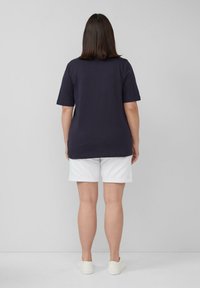 Marine-blaues T-Shirt mit kurzen Ärmeln, lockere Passform, kombiniert mit weißen Shorts. Einfaches Design, Baumwollmaterial, glatte Textur, getragen mit weißen Schuhen.