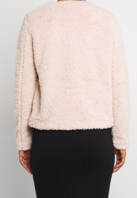 Lyserosa, blød og luftig plysjakke med lange ærmer og elastisk bundkant. Har et enkelt, hyggeligt design uden synlige lukninger.