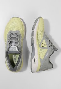 Des chaussures de sport légères jaunes et grises dotées de matériaux en maille et synthétiques, d'un système de laçage bien en vue et de semelles texturées avec des accents proéminents.