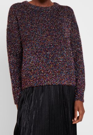 Pull en maille duveteuse multicolore à manches longues porté avec une jupe plissée noire sur une personne.