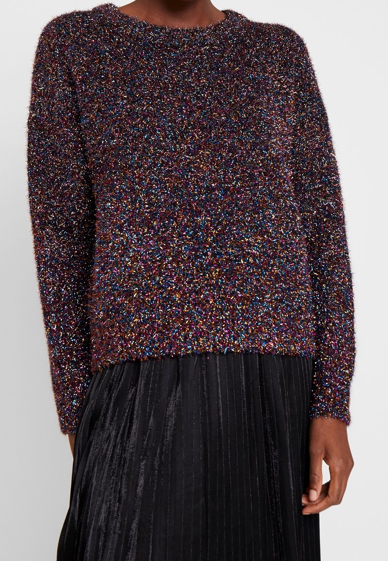 Pull en maille duveteuse multicolore à manches longues porté avec une jupe plissée noire sur une personne.