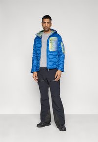 Μπλε μπουφάν με επένδυση και πράσινη τσέπη, γκρι μπλούζα, μαύρο παντελόνι με φερμουάρ και μαύρα παπούτσια. Λεία υφή, με κουκούλα.