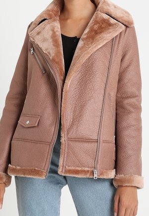 Braune Kunstlederjacke mit Schafslederkragen und -besatz, Reißverschluss vorne, Seitentaschen und strukturierter Oberfläche, getragen mit hellblauen Jeans.