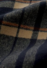 Tissu en laine douce avec un motif à carreaux bleu, beige et rouille, montrant la texture et les plis.