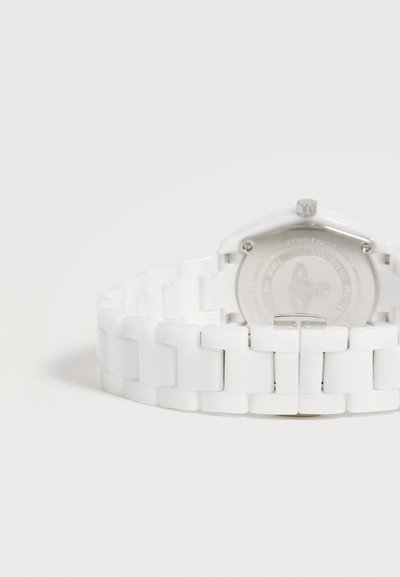 Bracelet de montre en céramique blanche avec fermoir en métal, vu de dos avec une partie du boîtier de la montre visible sur un fond blanc.