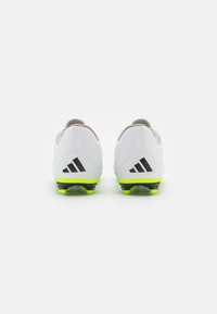 Botas de fútbol blancas con acentos grises, logotipo de tres rayas negras y suelas de un verde brillante. Presentan un diseño ligero y de perfil bajo.