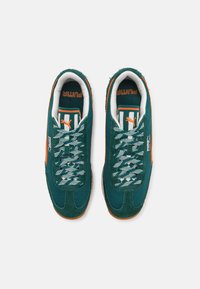 Zapatillas PUMA verdes y naranjas con parte superior de malla texturizada, detalles en ante y cordones estampados. Suelas de goma que proporcionan agarre.