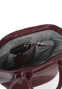 Bolso de mano de imitación piel en color burdeos con cierre de cremallera, que muestra un interior gris con patrones, compartimentos para gafas de sol, teléfono y bolígrafos.