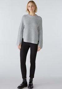 Pull en maille côtelée gris clair à manches longues et fentes sur les côtés, associé à un pantalon slim noir et des chaussures noires brillantes.