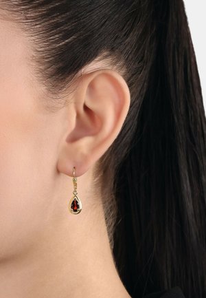 Orecchini a goccia in oro con pietra preziosa rossa a forma di goccia, che mostrano una finitura lucida e impostazioni a griglia intricate.