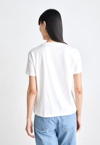T-shirt bianca in cotone con maniche corte e scollo rotondo. La vista posteriore mostra una vestibilità comoda e una superficie liscia. Abbinata a jeans azzurri chiari.