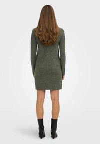 Vestito a maglia verde oliva con maniche lunghe, silhouette aderente, orlo a coste, abbinato a stivali neri alla caviglia. Materiale morbido e testurizzato.