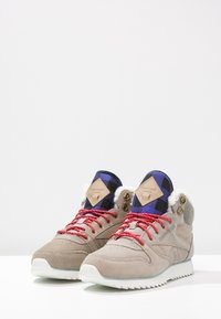Gray suede high-top sneakers with red laces, plaid accents, and faux fur lining; rubber sole with serrated traction for grip.