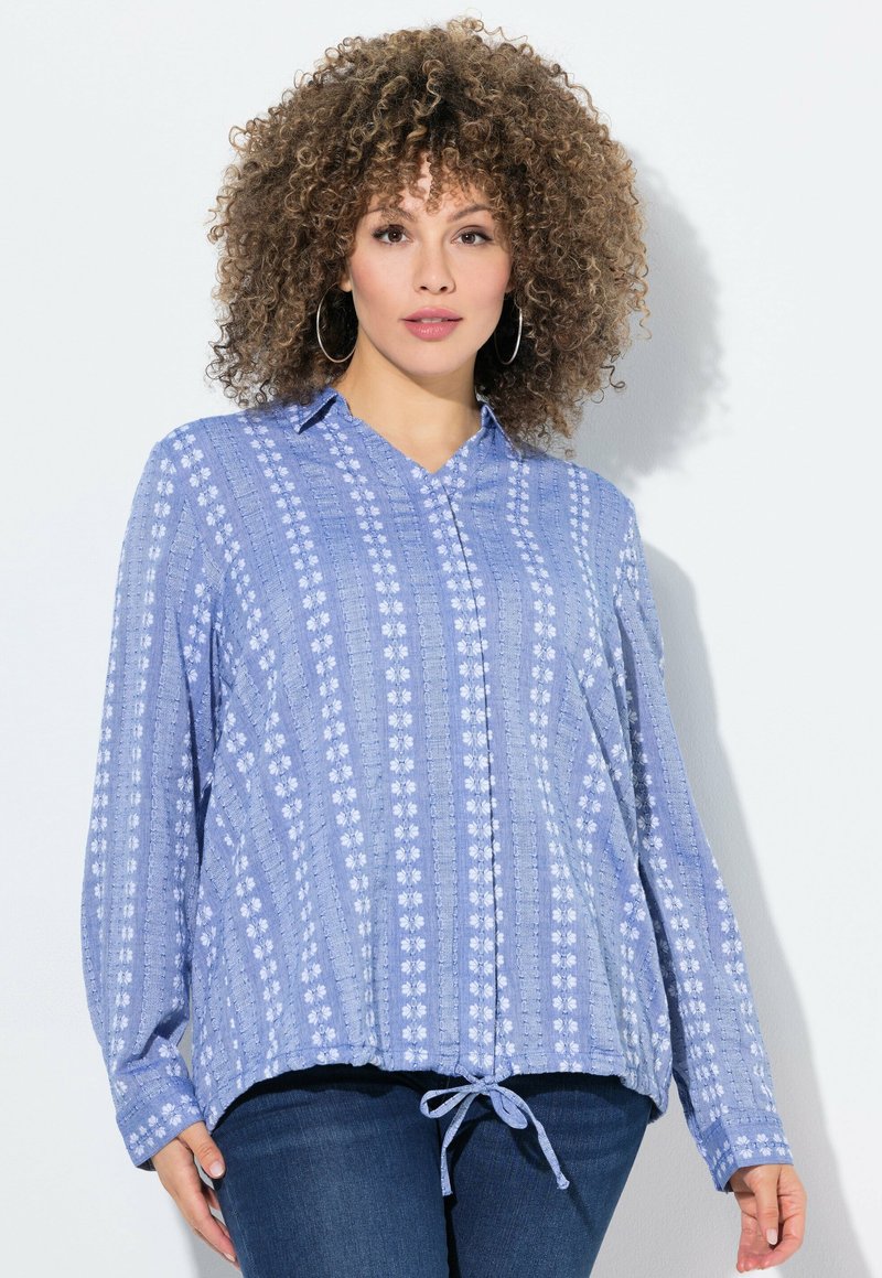 Blusa a maniche lunghe di colore azzurro chiaro con colletto, caratterizzata da un motivo floreale e coulisse all'orlo. Realizzata in un tessuto testurizzato.