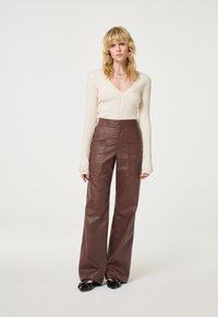 Roomkleurig geribd shirt met lange mouwen en V-hals, gecombineerd met high-waist bruine neplederen broek met opgestikte zakken en wijde pijpen.
