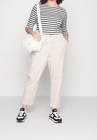 Stribet langærmet top, lyserøde bukser med afslappet pasform, hvid faux fur taske og sorte New Balance sneakers.