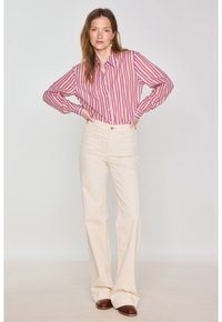 Camicia abbottonata con righe verticali rosa e bianche, abbinata a pantaloni a zampa d'elefante color crema. Scarpe marroni, tessuto liscio e vestibilità su misura.