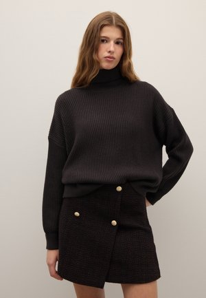 Maglione a collo alto a coste nere abbinato a una gonna scura con texture, caratterizzata da bottoni dorati e un taglio diagonale, creando un look a strati.