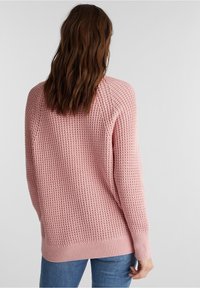 Roze gebreide trui met een textuurontwerp, lange mouwen en een ribbelboord. Draagt over blauwe jeans, met een loose fit.