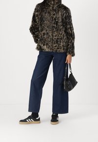 Giacca in pelliccia sintetica con stampa leopardata; jeans a vita alta blu scuro; sneakers nere con strisce bianche; piccola borsa nera con tracolla a catena.