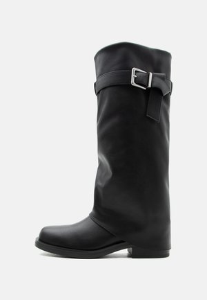 Hoher schwarzer Lederstiefel mit einem silbernen Schnallenriemen um den oberen Wadenbereich und einem niedrigen, quadratischen Absatz.